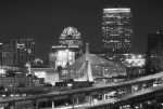 Black and white panoramic view of a city skyline at night with illuminated buildings and a curved freeway.