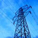 Electricity pylon against a blue sky with scattered clouds, power lines visible, low angle view.