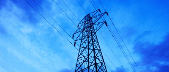 Electricity pylon against a blue sky with scattered clouds, power lines visible, low angle view.