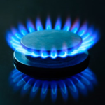 Blue flames emitting from a metal gas stove burner against a dark background.