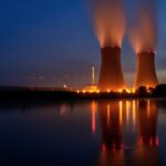 Nighttime view of a nuclear power plant with illuminated cooling towers reflecting in a calm river.