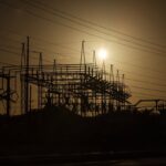 Sunset silhouetting an electrical substation with power lines and structures, creating a dramatic industrial landscape.