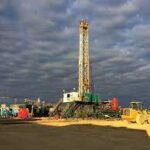 An oil drilling rig and associated equipment under a cloudy sky at a remote field location.