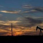 Silhouette of an oil pumpjack against a colorful sunset sky with orange and blue hues.