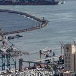 Aerial view of a port with cranes, a cargo ship, and parked vehicles.