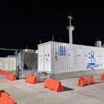 Industrial hydrogen generators installed on a rooftop, surrounded by orange safety barriers under clear night sky.