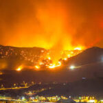 Here's an alt tag for the image: Large wildfire raging on a mountain at night.